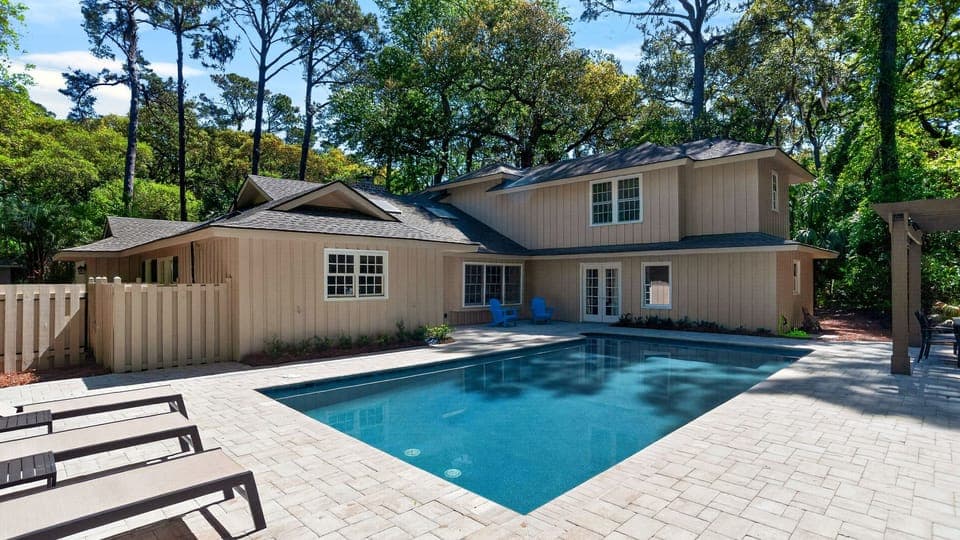 Sunny backyard escape with a modern two‑story home and a sparkling pool framed by tall trees.