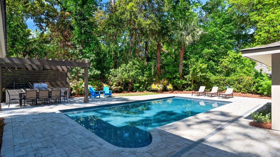 Serene backyard oasis with a modern pool, pergola dining, and lounge seating tucked into lush greenery.