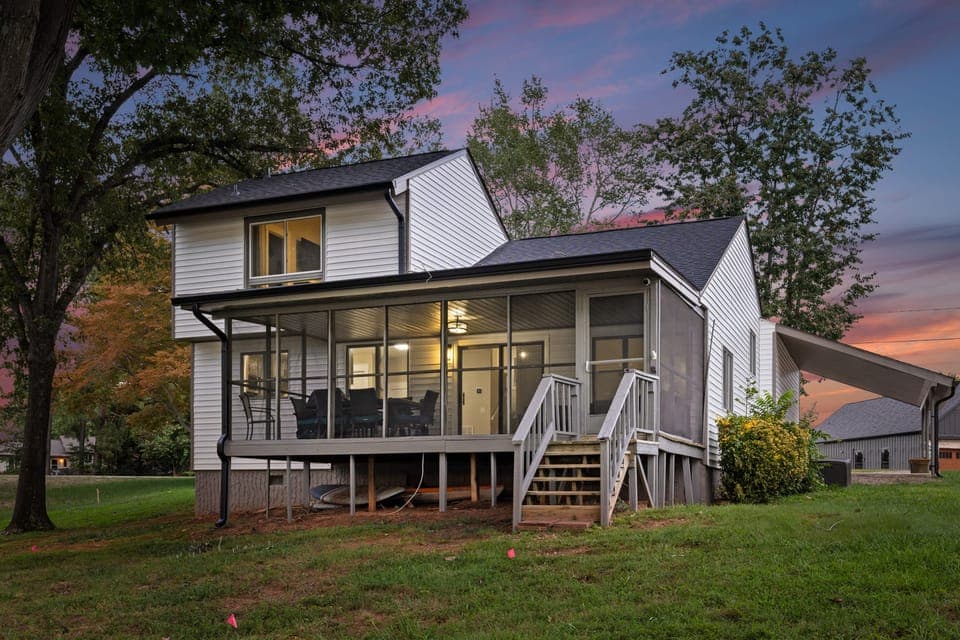 Charming exterior with a screened-in porch, set against a vibrant sunset sky.