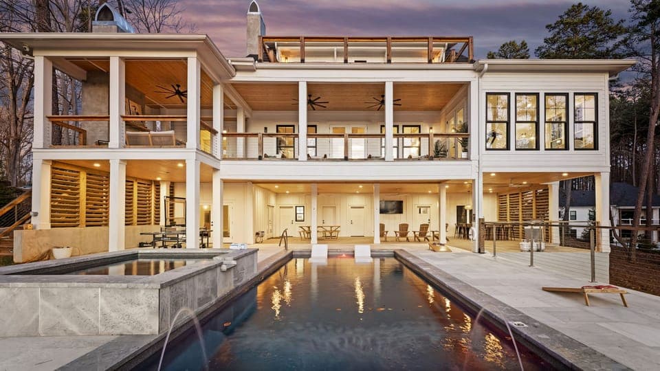 Modern lakeside home rear view at dusk with pool and balcony.