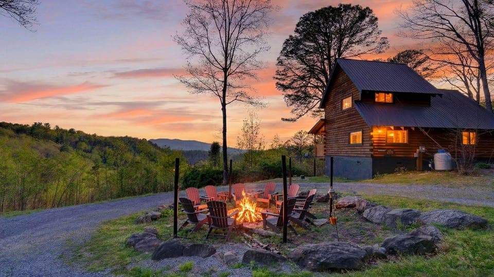 Hillside cabin with a glowing fire pit and Adirondack chairs, set against a colorful mountain sunset. (Isaiah's Cabin)