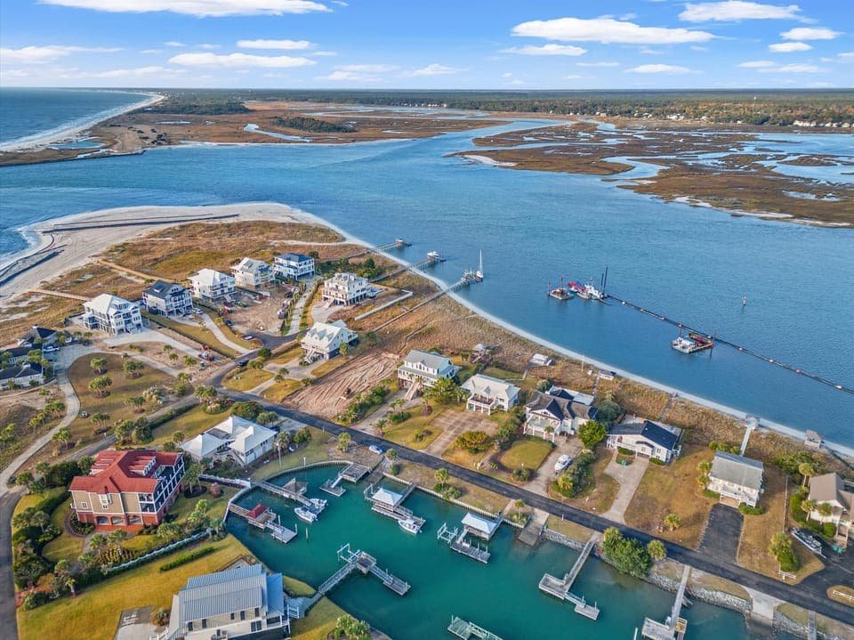 Aerial view of coastal community with waterfront homes, marina, and pristine waters flowing toward the ocean.
