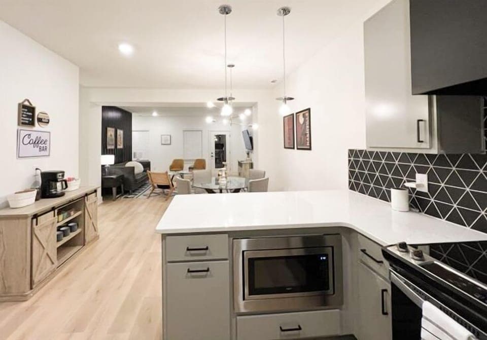 KITCHEN – This kitchen open to the living area is sleek and modern designed for both style and functionality. The black geometric backsplash adds a bold touch, contrasting beautifully with the soft grey cabinetry and white countertops. Stainless steel appliances, including a large refrigerator, dishwasher, and a handy toaster oven, make meal prep and cleanup a breeze. With plen...