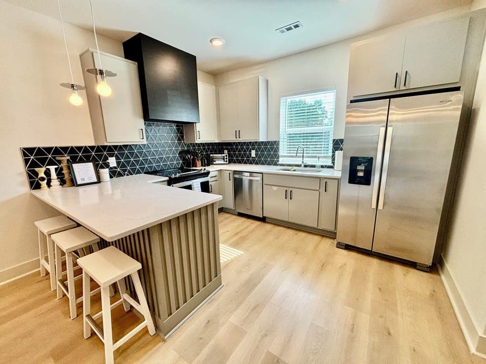 KITCHEN – Fully Equipped Modern Kitchen with Stainless Steel Appliances for a Home-Cooked Meal Experience in Nashville. Sleek and functional, this modern kitchen offers the perfect blend of style and practicality. The striking black geometric backsplash contrasts beautifully with the light grey cabinetry, creating a bold yet elegant look. A spacious white quartz countertop doub...