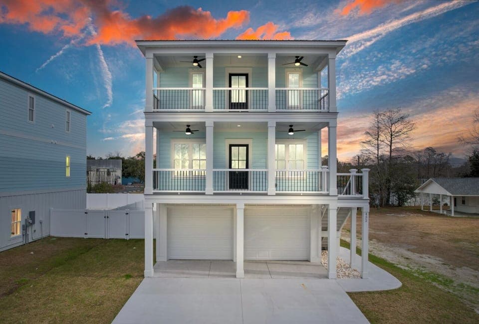 Charming three-story coastal home set against a stunning sunset sky in a peaceful residential neighborhood.