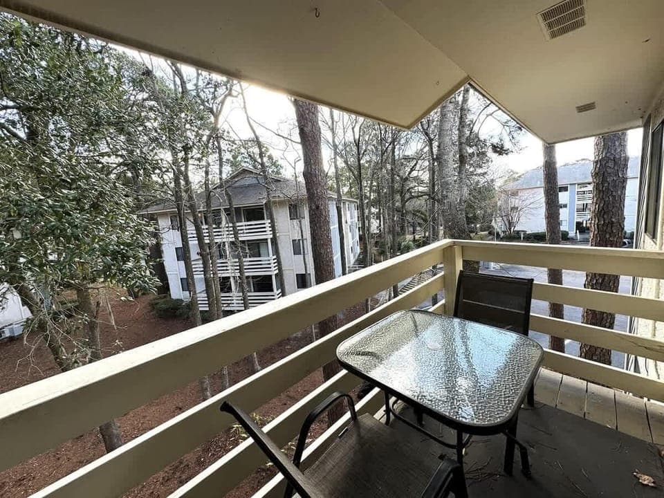 A cozy outdoor retreat with a glass-top table and chairs, in a wooded landscape.