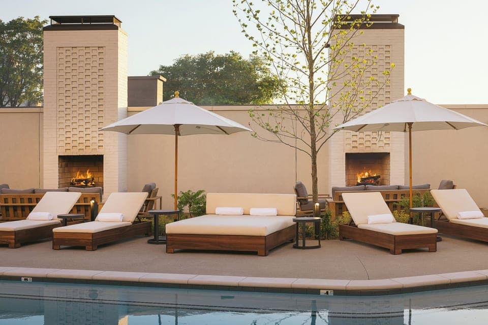Lounge poolside with cozy daybeds and glowing fire features.