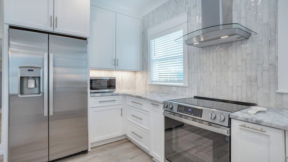 Crisp white cabinetry, marble countertops, and tile backsplash create a bright, polished look. Stainless steel appliances—including a contemporary range with a glass hood.