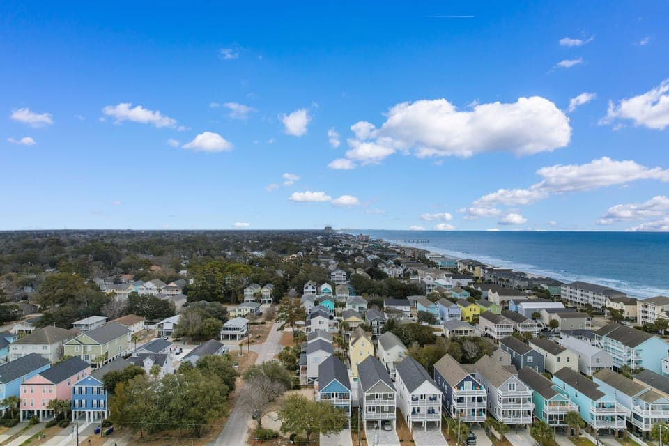 Aerial view of charming coastal neighborhood with colorful beach houses nestled between lush trees and pristine oceanfront.