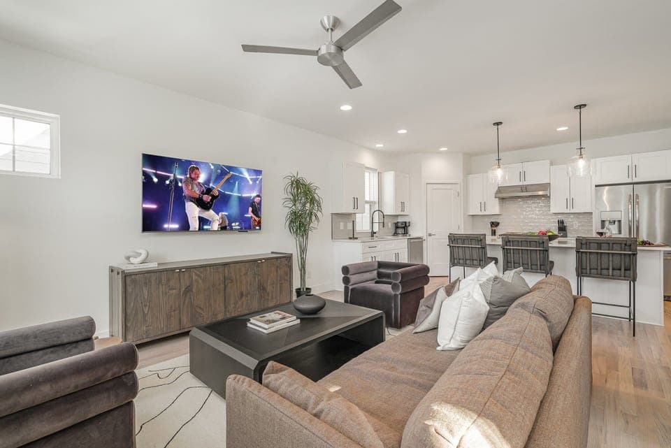 Relax in the cozy living room with ample seating, a flat-screen TV, and natural light pouring through large windows.