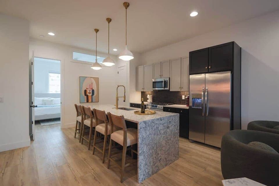 Modern kitchen with a marble island, bar seating, and stainless steel appliances.