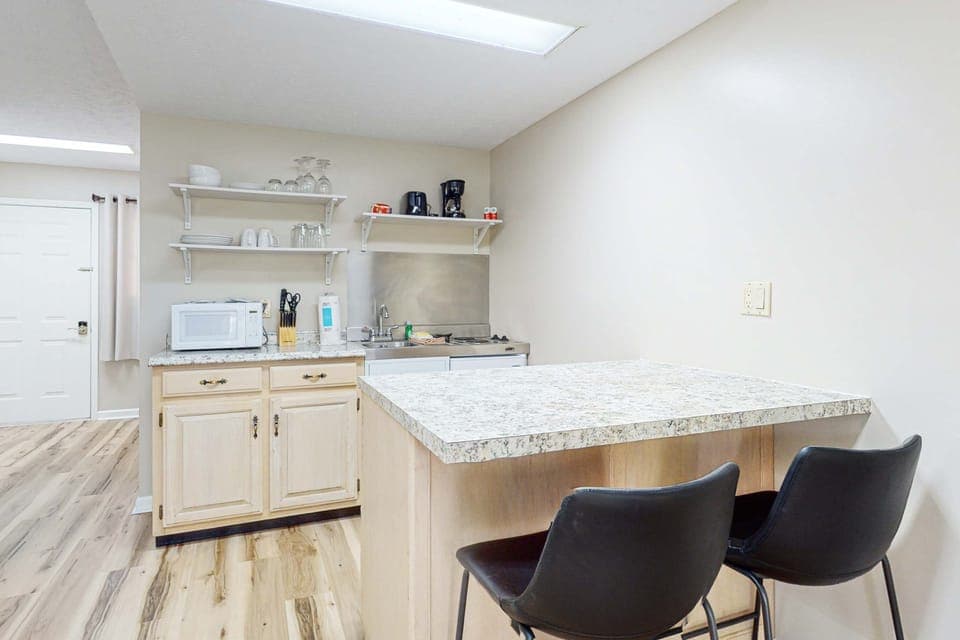 Kitchenette with breakfast bar seating, microwave, sink, cooktop, and coffee setup. Perfect for long stays and quick meals. Budget-friendly space with practical amenities and comfort.