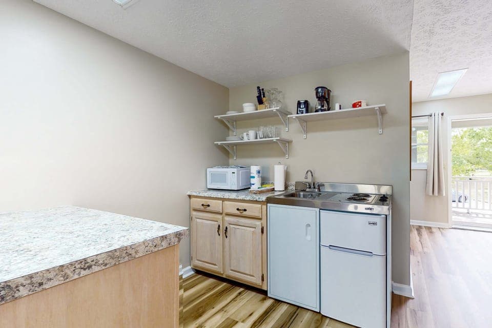 Stocked kitchenette with sink, cooktop, mini fridge, microwave, and coffee setup. Perfect for extended stays. Complete with studio amenities for easy meals, long-term lodging, and guest-friendly convenience.