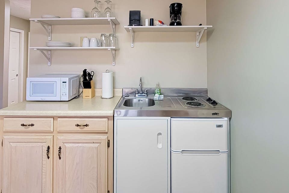Kitchenette with cooktop, mini-fridge, microwave, coffee maker, sink, dishes & glassware. Perfect for extended stay, work travel, golf getaway, and budget-friendly lodging with easy meal prep.