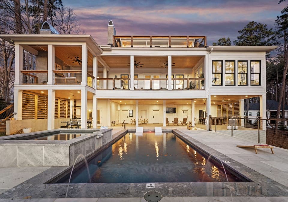 Modern lakeside home rear view at dusk with pool and balcony.