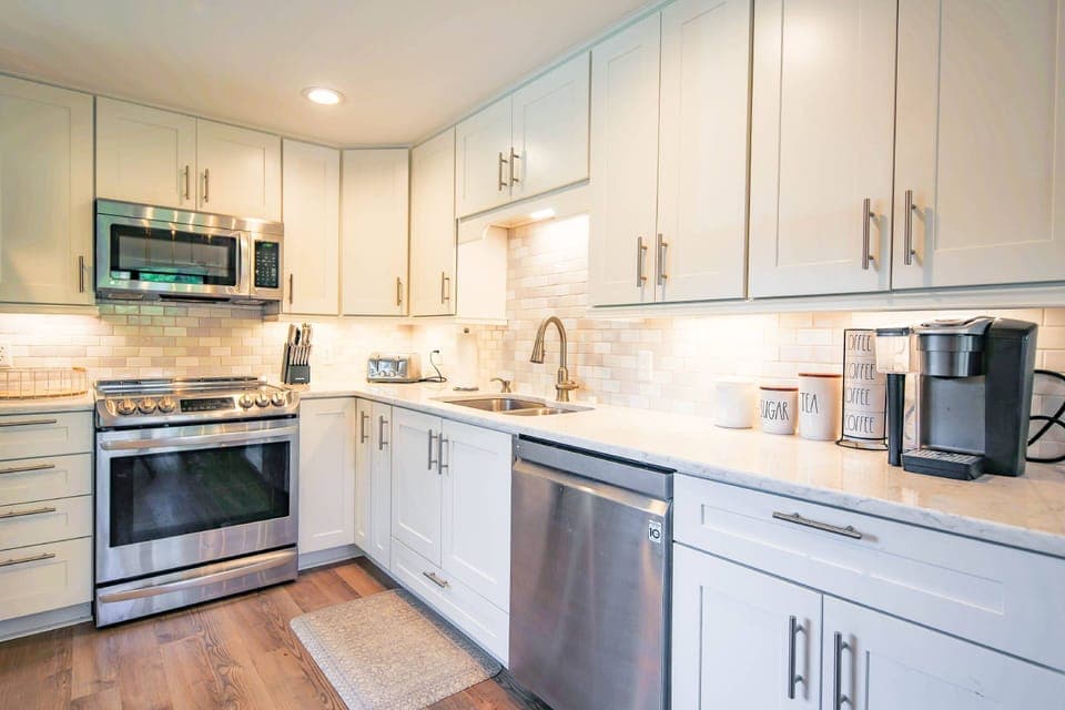 This gorgeous kitchen features white cabinetry, stainless steel appliances and a tiled backsplash.