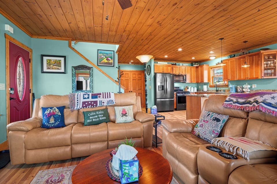 Cozy cabin living room with wood trim, turquoise walls, recliners, and kitchen.