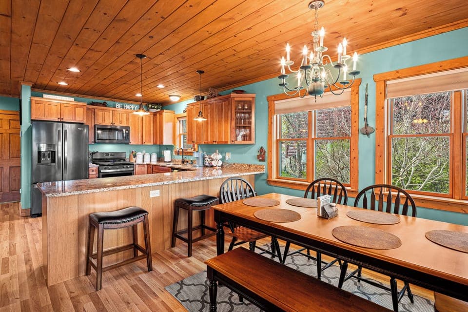 Warm cabin kitchen with wood cabinets, island, dining table, windows, trees view
