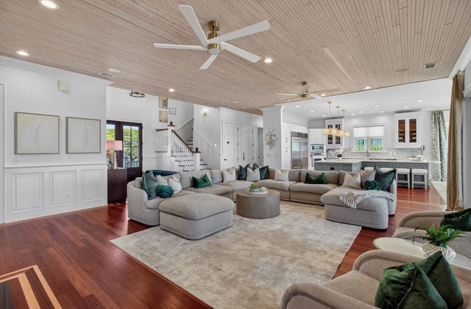 Sink into plush sectional seating surrounded by coastal elegance, where rich hardwood floors and soaring wood ceilings create your perfect gathering space.