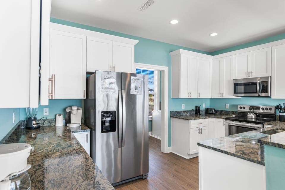 Cook with ease in your spacious kitchen featuring granite counters, stainless appliances, and cheerful turquoise walls that create a bright, welcoming atmosphere.