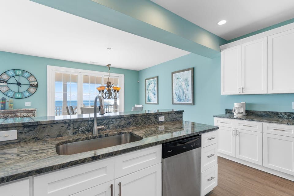 Your coastal kitchen features stunning marble countertops and gleaming white cabinets, with ocean views through the French doors.