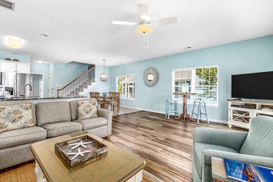 Relax in this spacious living area featuring comfortable seating, coastal accents, and an open kitchen perfect for entertaining.