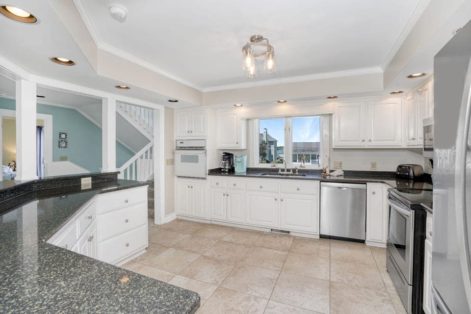 Your spacious kitchen features elegant white cabinetry, granite countertops, and stainless steel appliances, perfect for preparing meals with ocean views.
