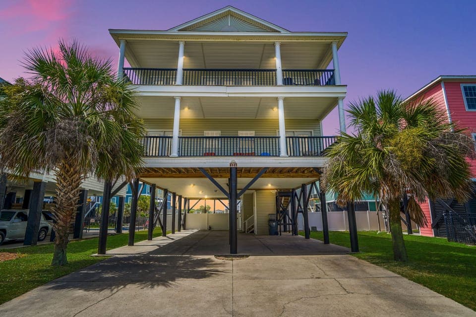 Beautiful coastal home with covered parking and tropical palm trees, captured during a stunning sunset in a charming beachside neighborhood.