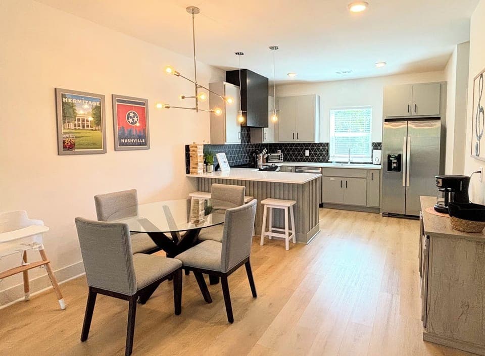 KITCHEN & DINING AREA – This modern kitchen and dining space offers both style and functionality. The sleek glass dining table is complemented by comfortable upholstered chairs, perfect for family meals or casual gatherings. The kitchen features stainless steel appliances, chic cabinetry, and a striking black geometric backsplash. Pendant lighting above the island adds a contem...