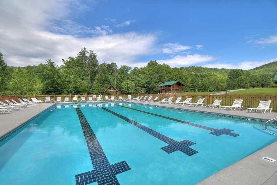 Outdoor swimming pool with lounge chairs set against a forested mountain backdrop