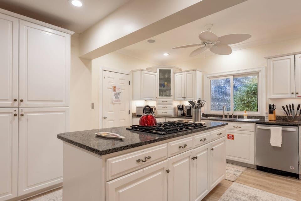 A modern kitchen with white cabinets, a built-in oven, a gas stove, and a large granite island.