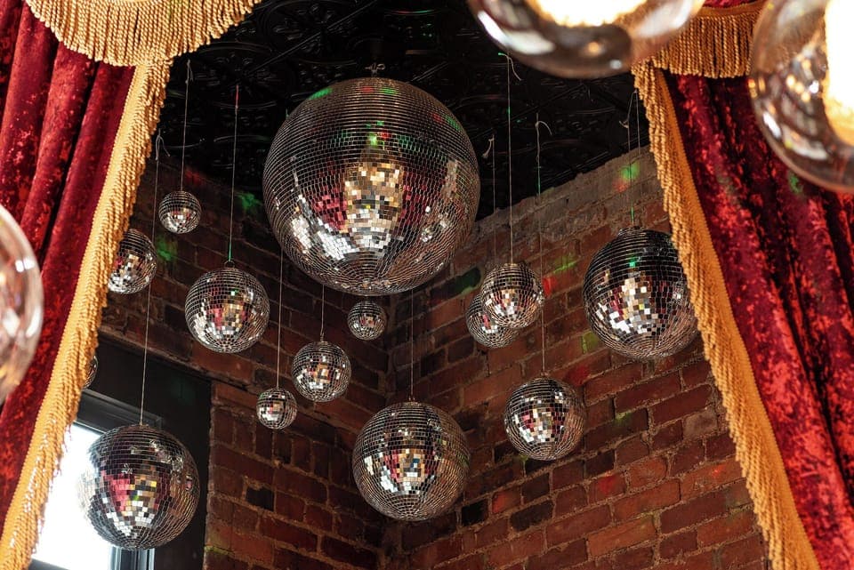 - Cluster of disco balls shining against brick walls   - Dramatic velvet drapes frame this glowing statement corner   - Perfect photo spot adding sparkle and vintage party vibes