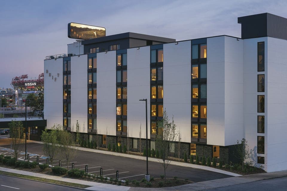 Arrive effortlessly to a sleek, modern hotel exterior at dusk.