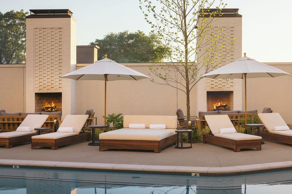 Lounge poolside with cozy daybeds and glowing fire features.