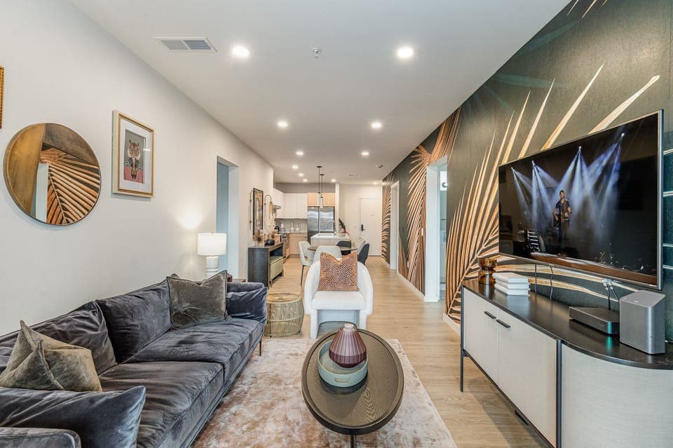 Unit 1: Warm and inviting living space featuring a large flat-screen Smart TV and designer furnishings with a spacious balcony.