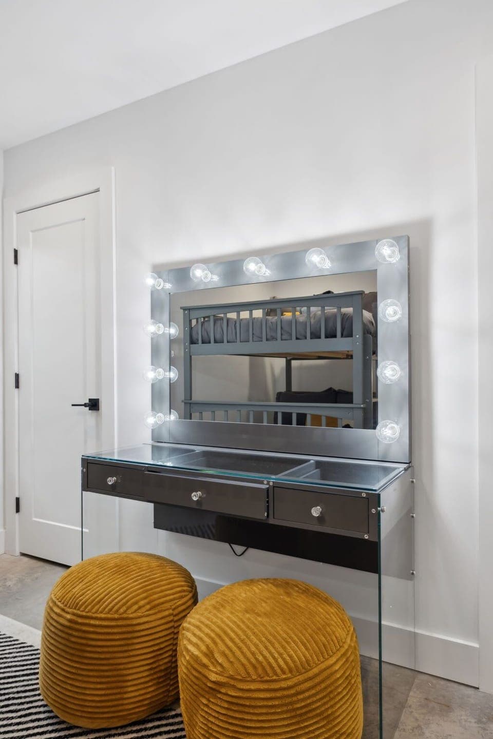 Bedroom 2: Elegant glam station with a mirror framed by lighting and modern, plush seating.