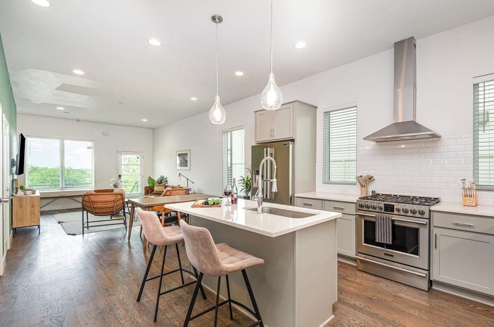 Unit 1: Bright open-concept kitchen featuring a quartz-topped island with bar seating, stainless steel appliances, and abundant natural light streaming through the windows.