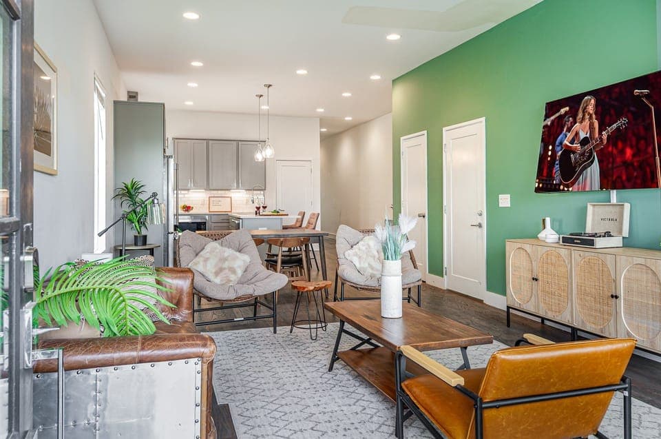 Unit 1: Welcoming living area with a vibrant green accent wall, large Smart TV, and plush seating arranged to take in the serene outside views.