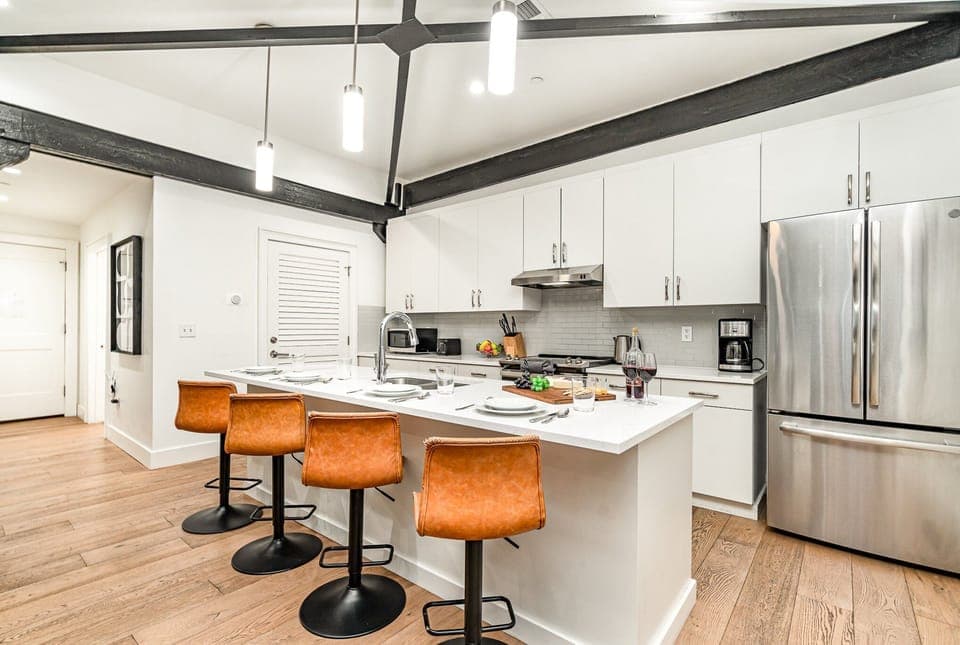 Unit 2: Kitchen with stainless steel appliances, white cabinetry and countertops, and kitchen island with bar seating for 4 guests.