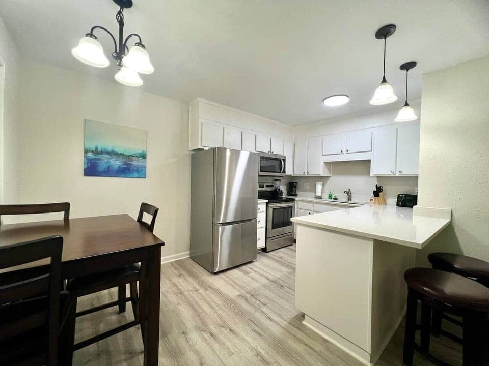 This fully equipped kitchen features stainless steel appliances, a large counter with seating, and a cozy dining nook framed by natural light. Whether you’re cooking a full meal or enjoying takeout, this space is perfect for gathering and dining in.