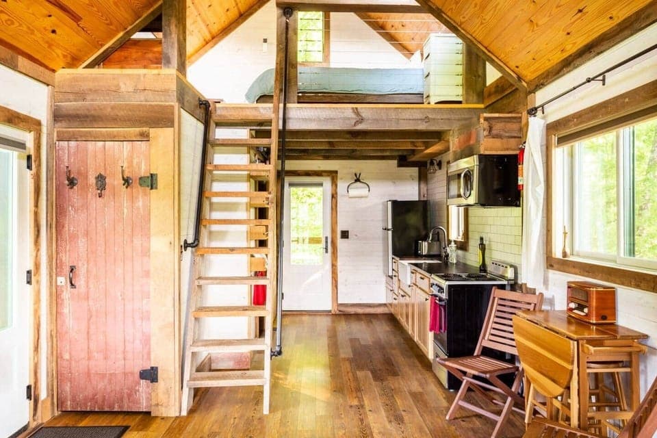 Entrance door on the left. red barn closet door. view into kitchen. ladder to loft with queen bed. 
