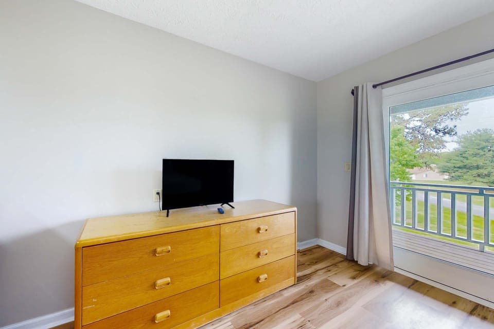 Smart TV on dresser with balcony access. Relax after exploring, golfing, or hiking. Comfortable, simple studio setup with natural light, fresh air, and space to unpack.