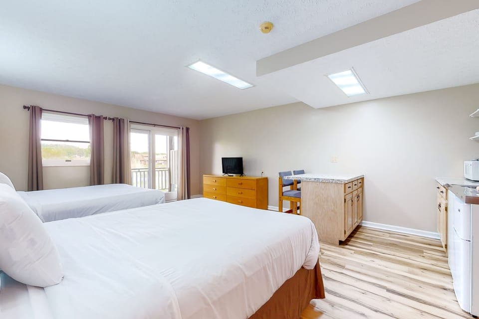 Bright studio suite with 2 queen beds, kitchenette, dining bar, and TV. Ideal for getaway, family trip, weekend escape, or extended stay with easy meal prep and comfy sleep space.