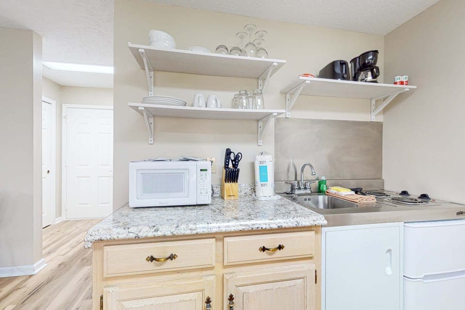 Kitchenette with microwave, sink, cooktop, mini fridge, dishes, and coffee maker. Everything for simple meals. Ideal getaway setup for extended stays, families, and weekend travelers.