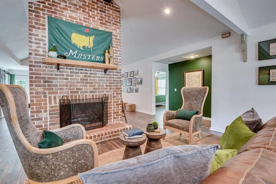 Cozy living room with a brick fireplace, stylish armchairs, and green accents, perfect for relaxing.