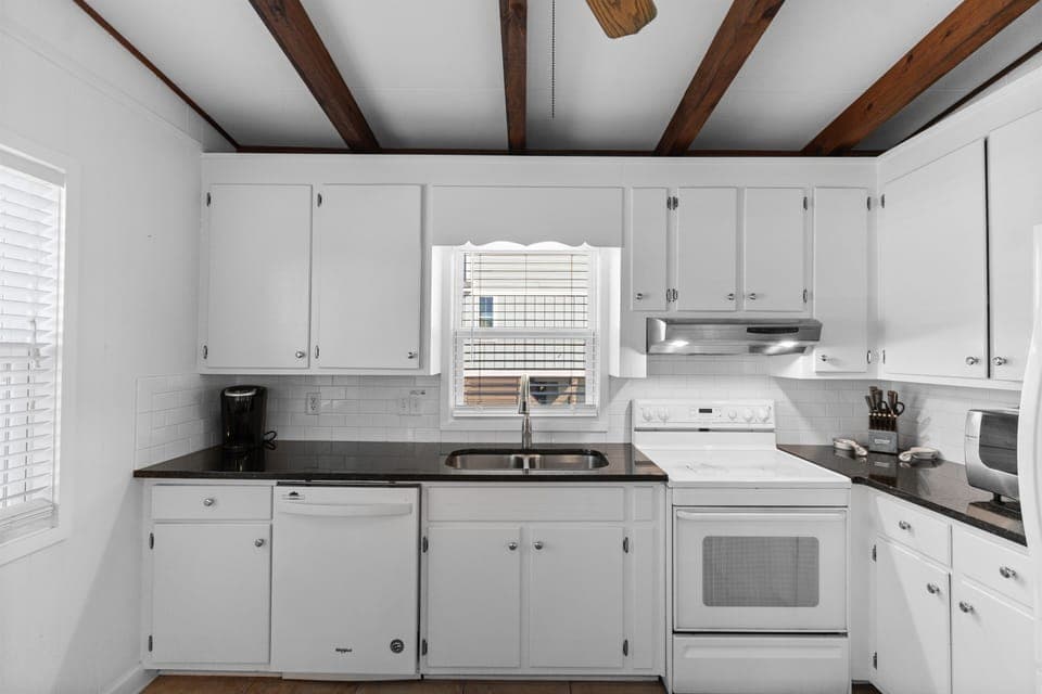 Cook your favorite meals in this bright, fully-equipped kitchen featuring white cabinetry, dark countertops, and charming exposed wooden ceiling beams.