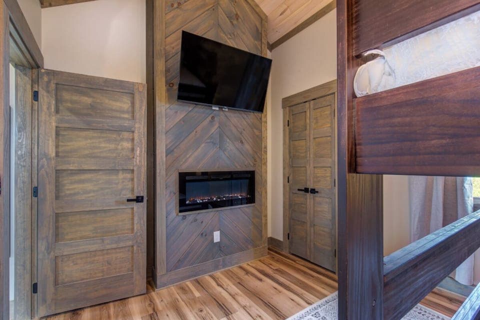 Cozy up in your rustic bedroom featuring a stunning chevron wood fireplace, flat-screen TV, and beautiful hardwood floors for ultimate relaxation.