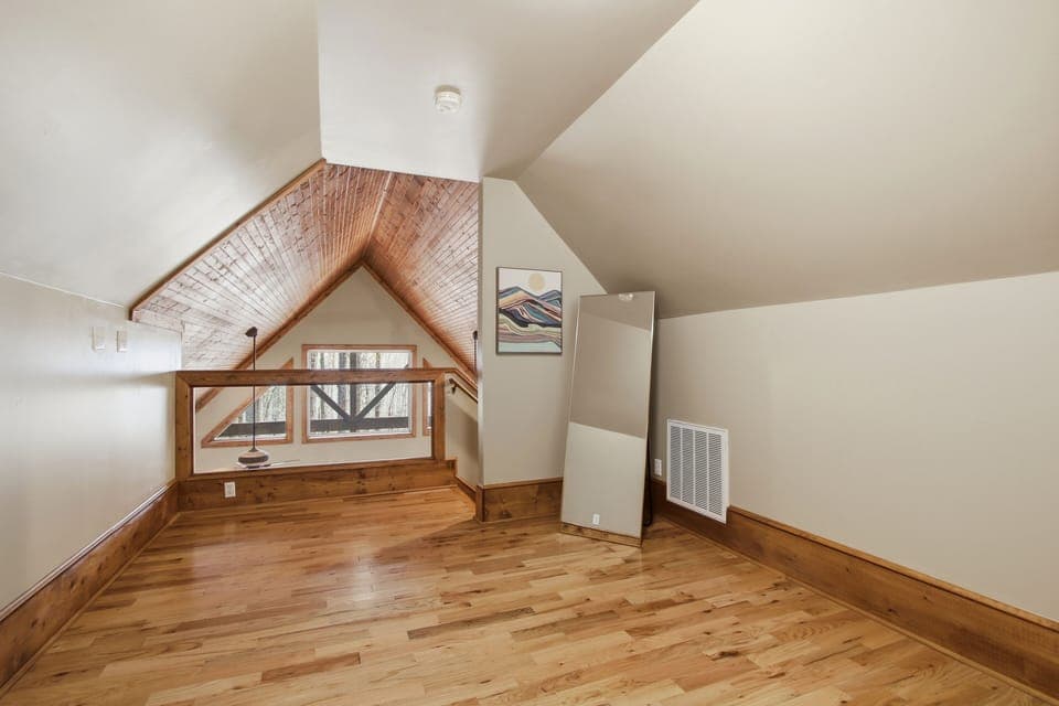 Loft with vaulted A-frame ceiling, hardwood floors, and mountain art