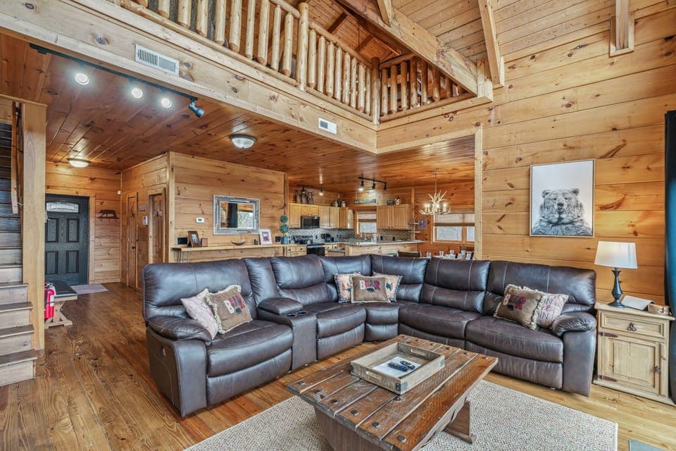 Relax in your spacious cabin living room with plush leather seating and rustic wood beams creating the perfect mountain retreat atmosphere.