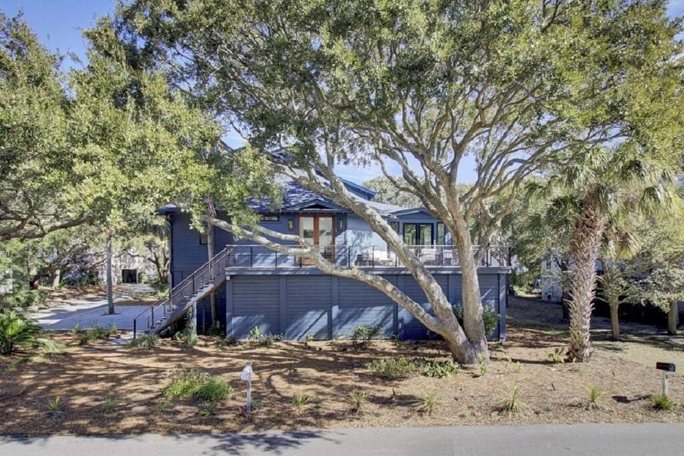 Elevated coastal home shaded by mature trees, with a spacious front deck and private stairs.